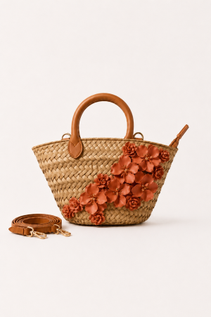 Woven straw tote bag with brown leather handles, detachable strap, and decorative orange floral details on a white background